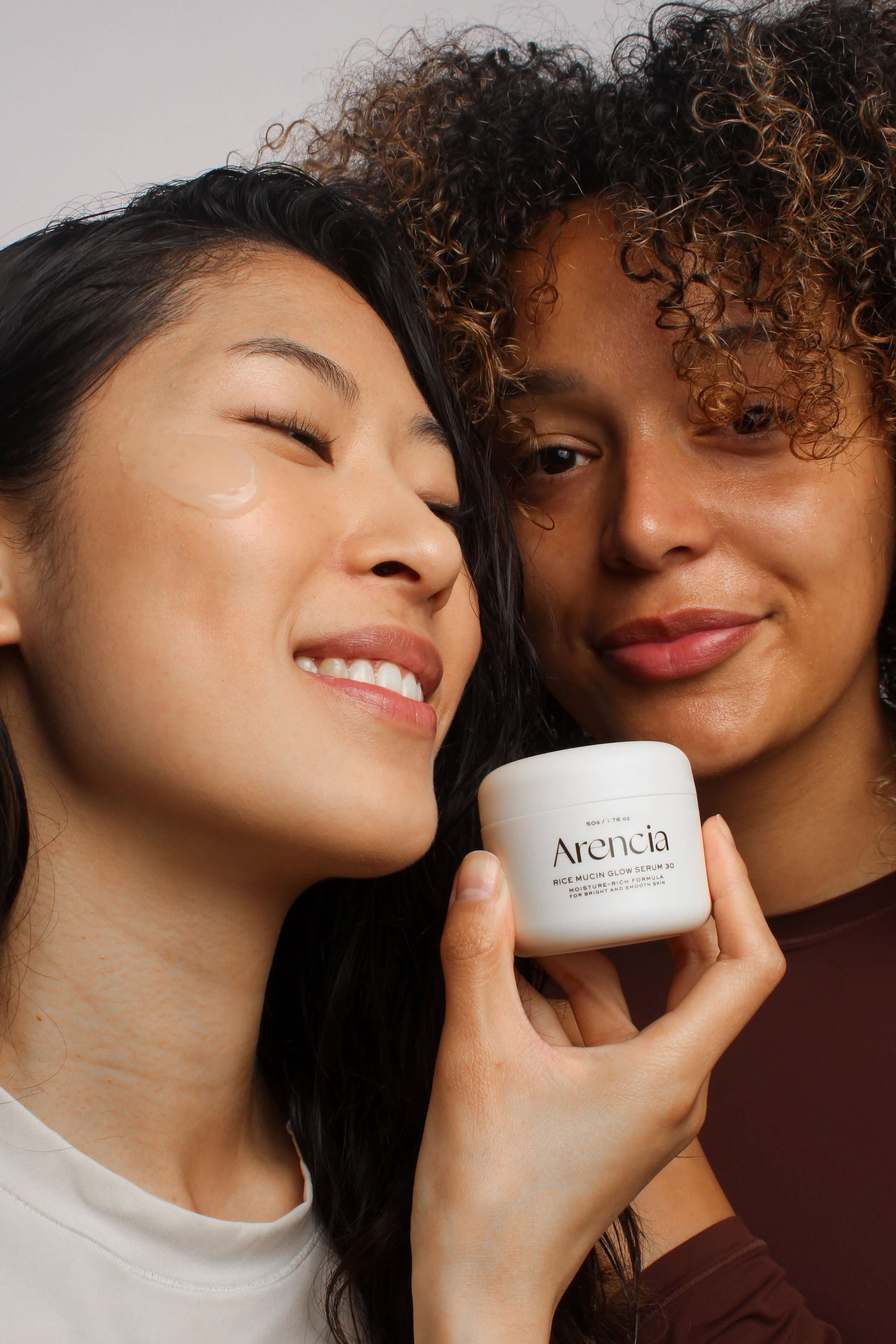 Deux mannequins souriants tenant le pot du sérum Arencia à la mucine de riz, adapté à toutes les carnations