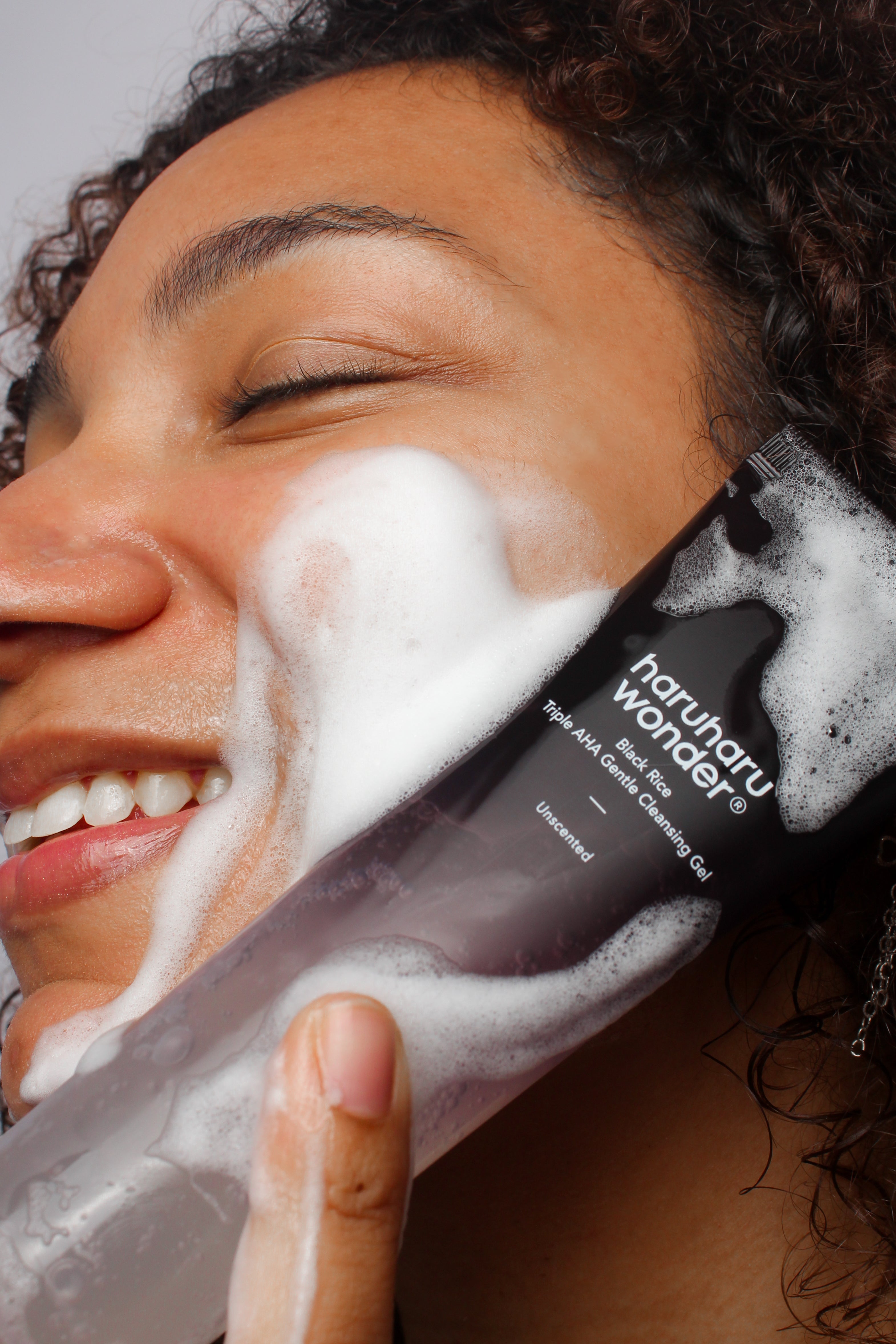 Mannequin utilisant le gel nettoyant doux triple AHA au riz noir Haruharu Wonder, mousse visible et tube en main