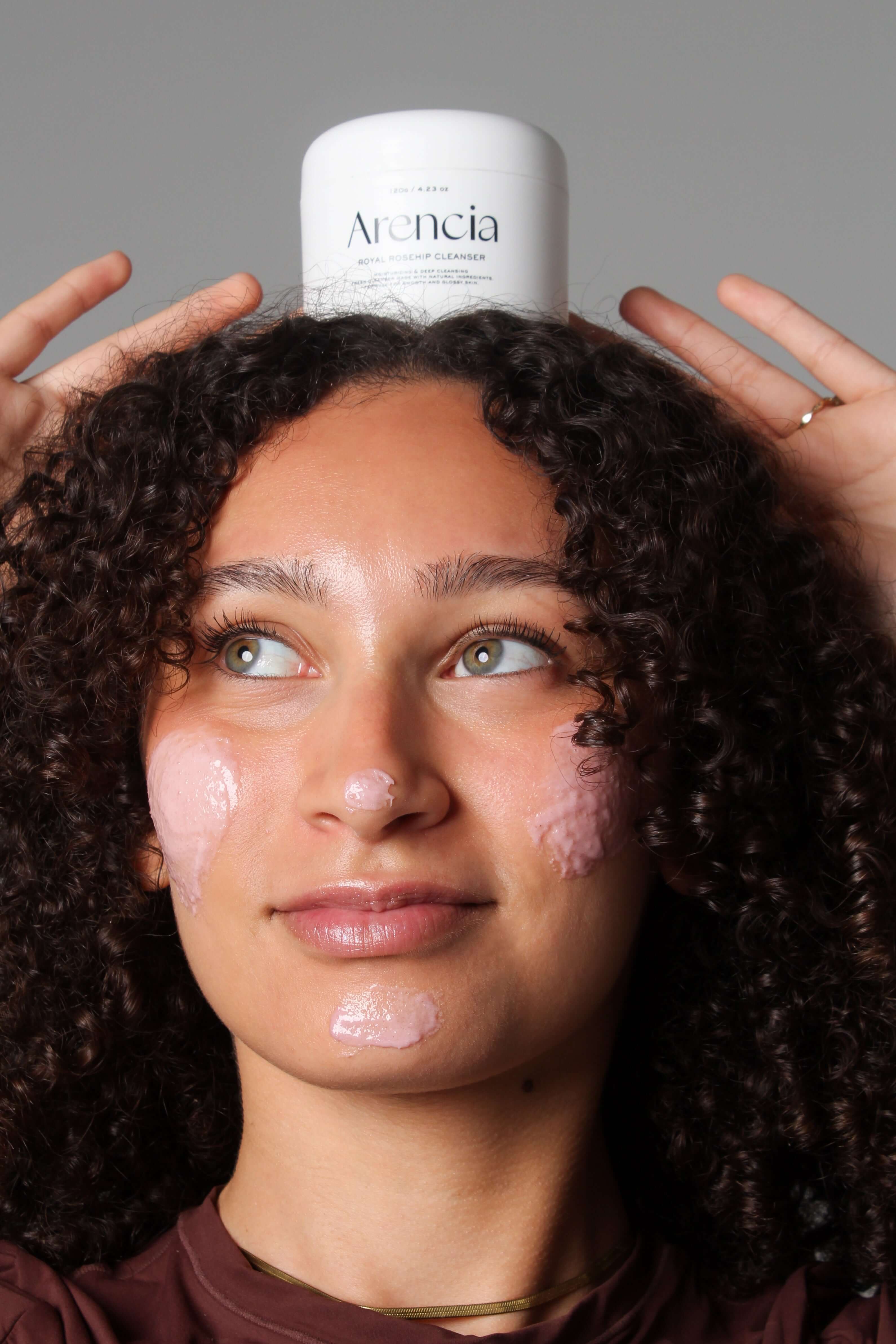 Mannequin souriant avec le nettoyant Arencia riz et églantier posé sur la tête, soin visage fun et naturel